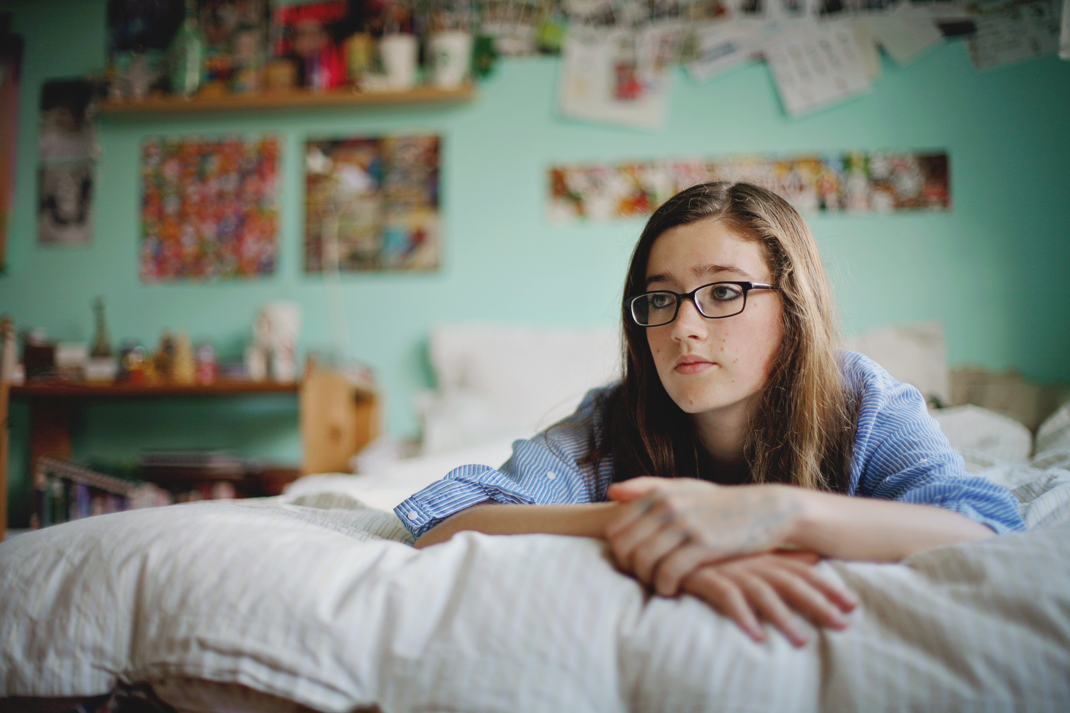 Teen girl wearing glasses laying on her bed in her room